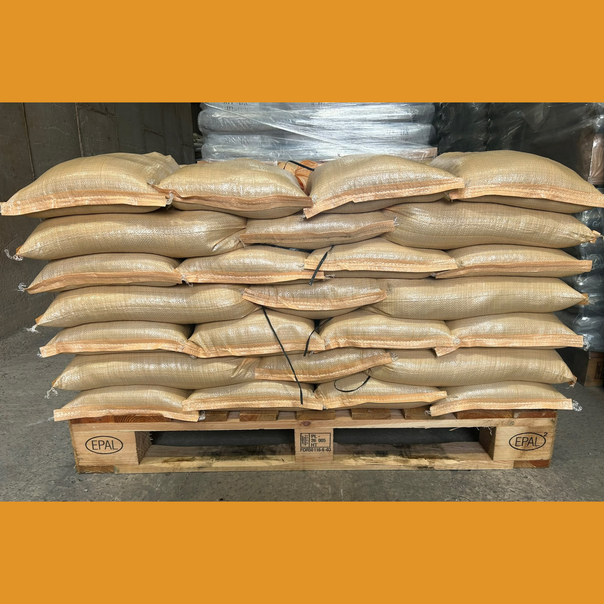 A wooden pallet stacked with flood defence sandbags photographed in a warehouse setting.